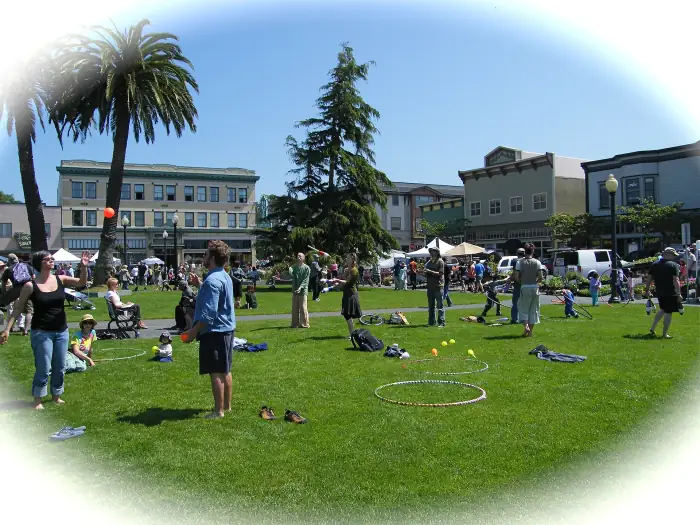 A busy farmers' market day on the Arcata Plaza, with jugglers on the lawn, palm trees and the Hotel Arcata behind