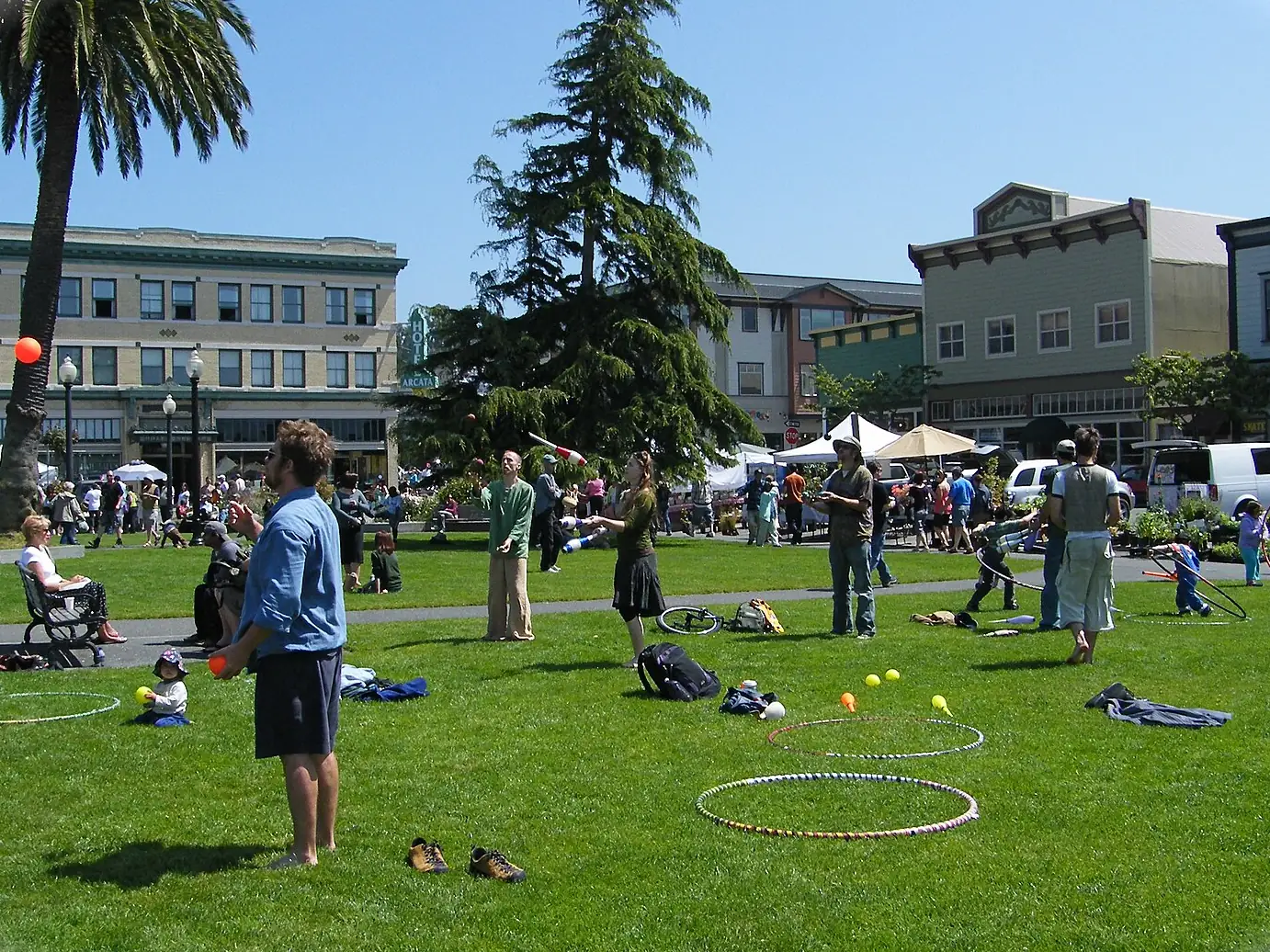 A busy farmers' market day on the Arcata Plaza, with jugglers on the lawn, palm trees and the Hotel Arcata behind