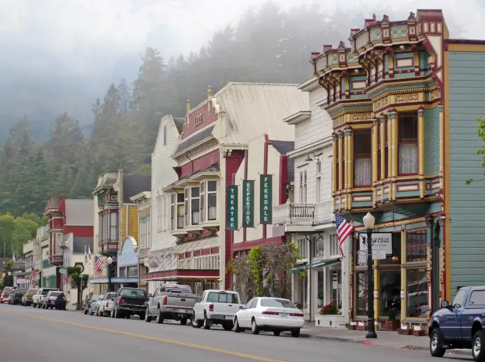 Victorian storefronts along Main Street in Ferndale with fog on the forested hill behind town