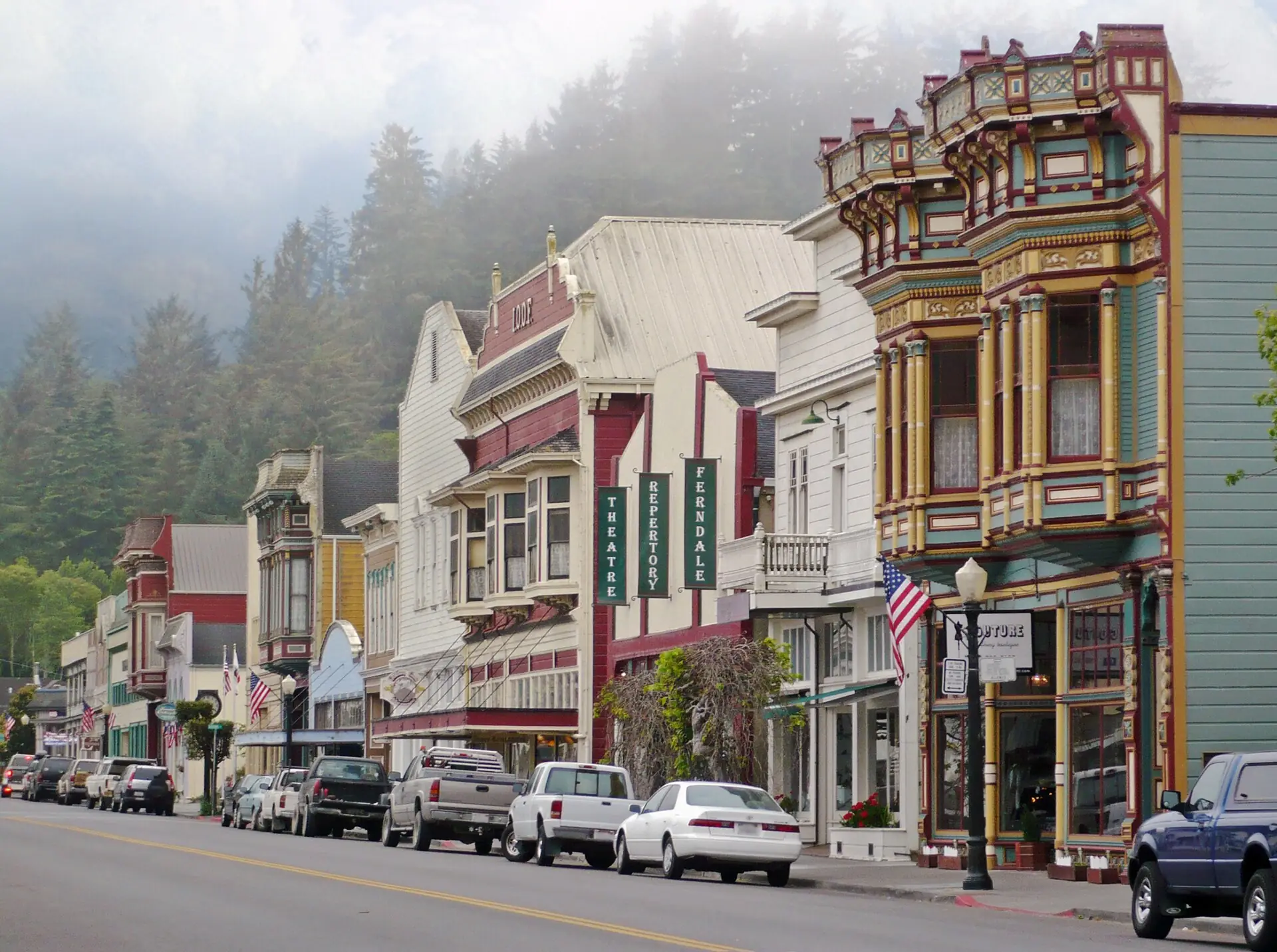 Victorian storefronts along Main Street in Ferndale with fog on the forested hill behind town