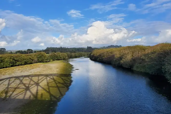 The Mad River curving between wooded banks at McKinleyville under a big blue sky, the Hammond Trail trestle casting its shadow on the gravel bar