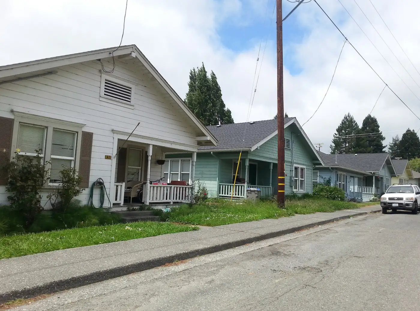 A row of former mill-company cottages in Scotia with front porches, small lawns and redwoods behind