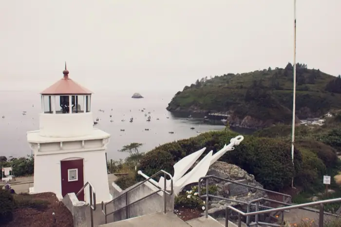 The white Trinidad Memorial Lighthouse above the harbor, fishing boats moored in the bay below Trinidad Head